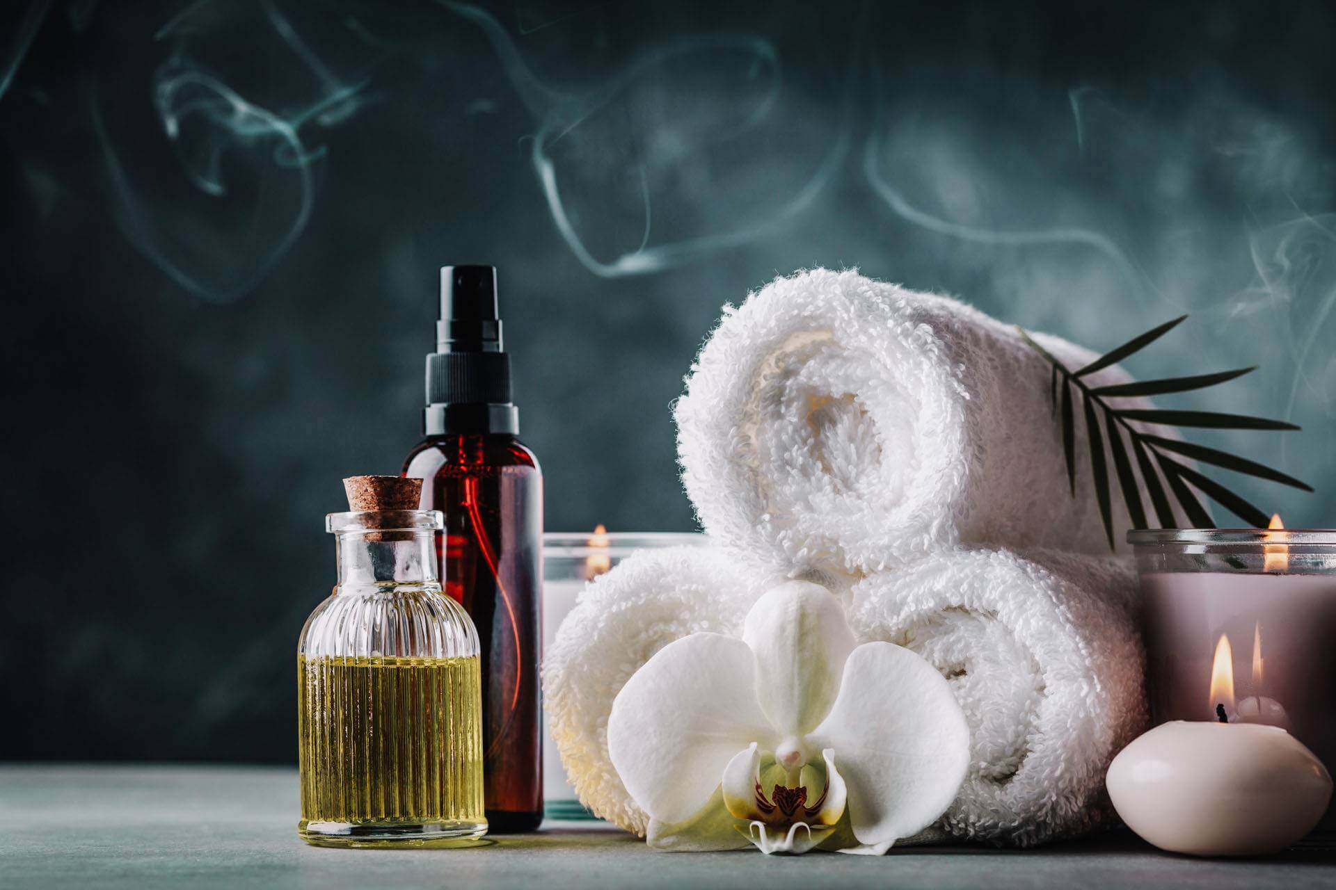 Aromatherapy, spa, beauty treatment and wellness background with massage oil, orchid flowers, towels, cosmetic products and burning candles.