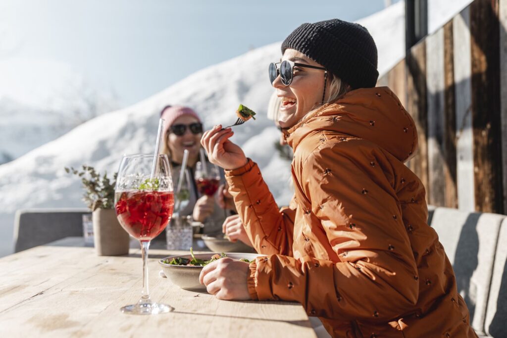Skifahrerein geniesst ihren Salat auf der Terasse einer Skihütte